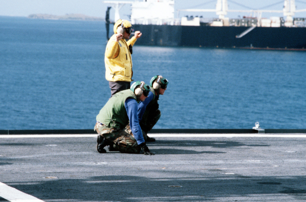 Two Marine Flight Deck Crewmen Stand By As The Plane Director Aboard