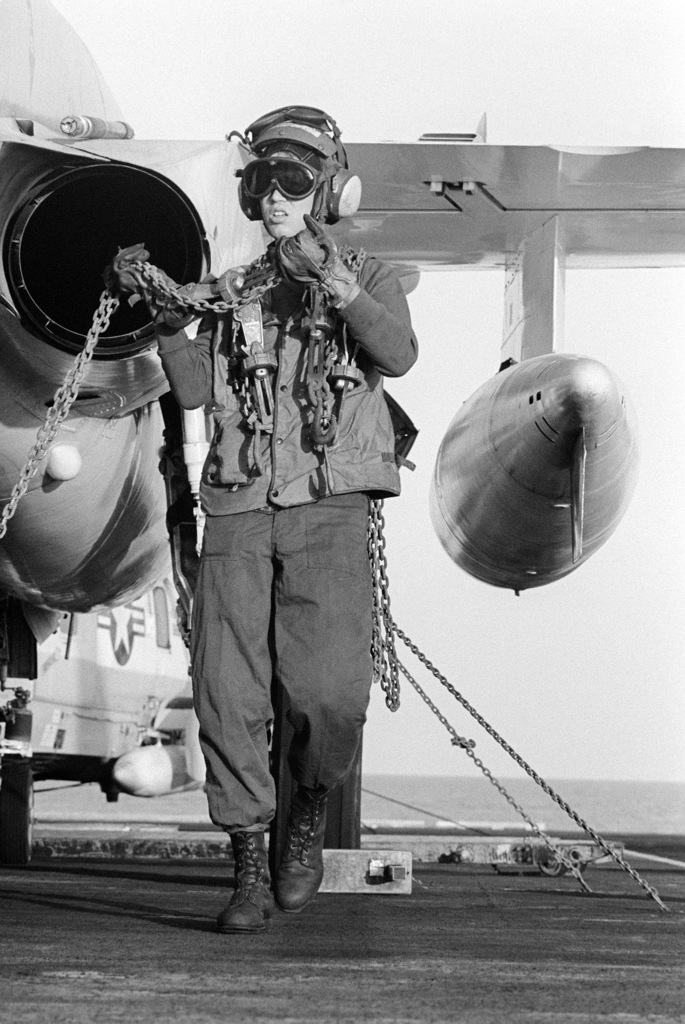 A flight deck crewmen uses tie-down chains to secure an A-6