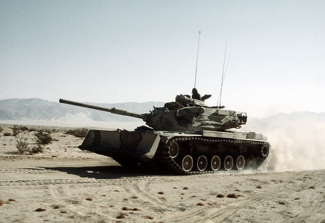 An M-60A1 tank, with an earthmover on its front, travels at a moderate ...