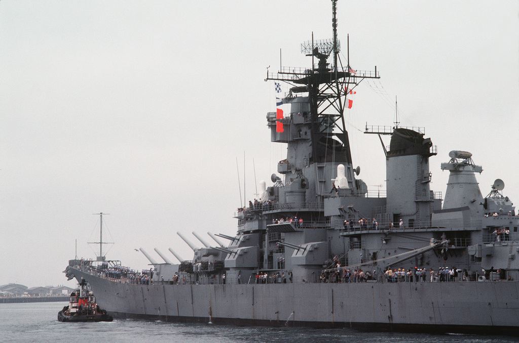 A tug boat, at the port bow, maneuvers the battleship NEW JERSEY (BB-62 ...