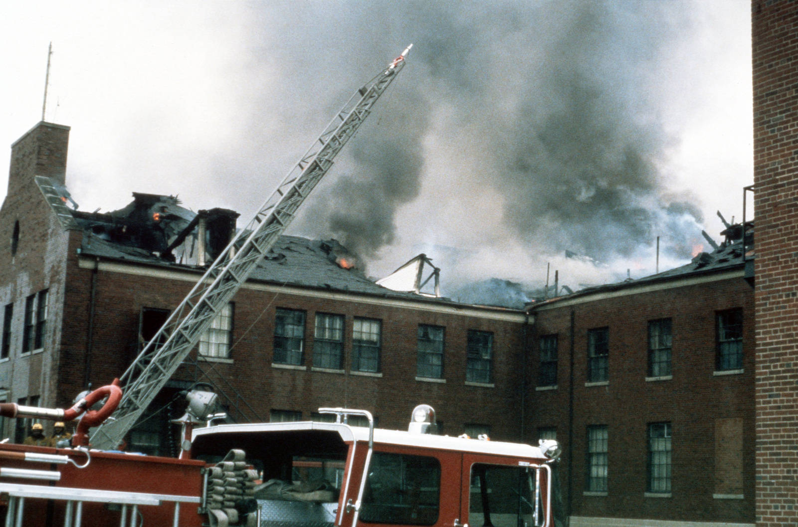 A ladder on a hook and ladder truck is extended above the gutted roof ...