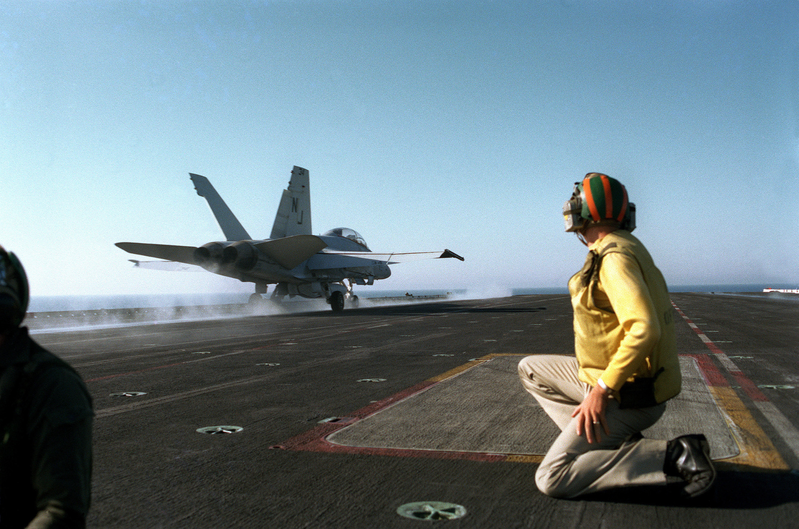 A flight deck crewman watches an F/A-18 Hornet aircraft take off from ...