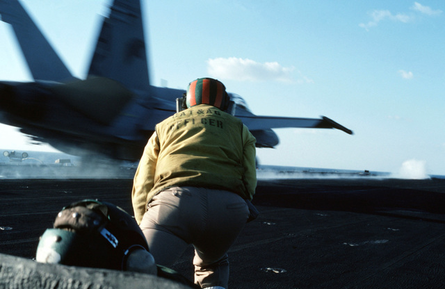 A catapult and arresting gear officer crouches on the flight deck of ...