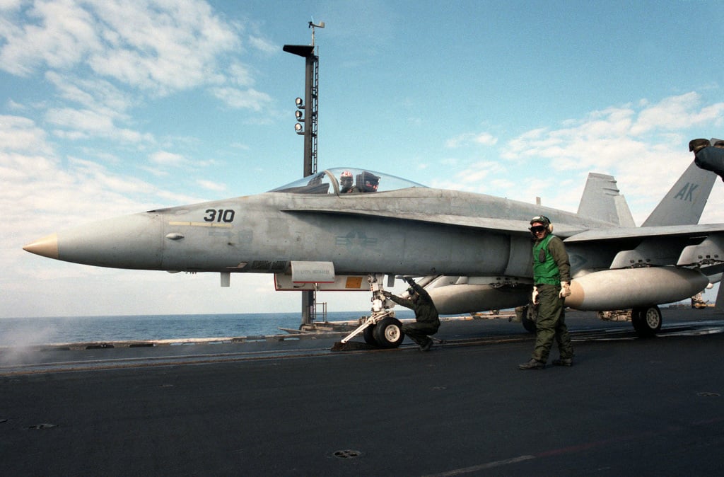A catapult crewman checks the catapult connections on an F/A-18A Hornet ...