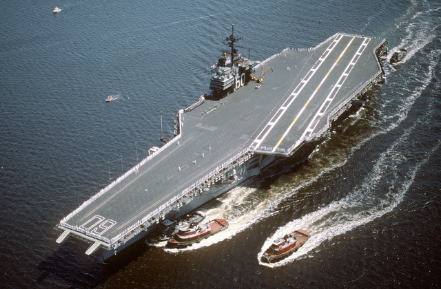 Crew members man the rail as tugs assist the aircraft carrier USS ...