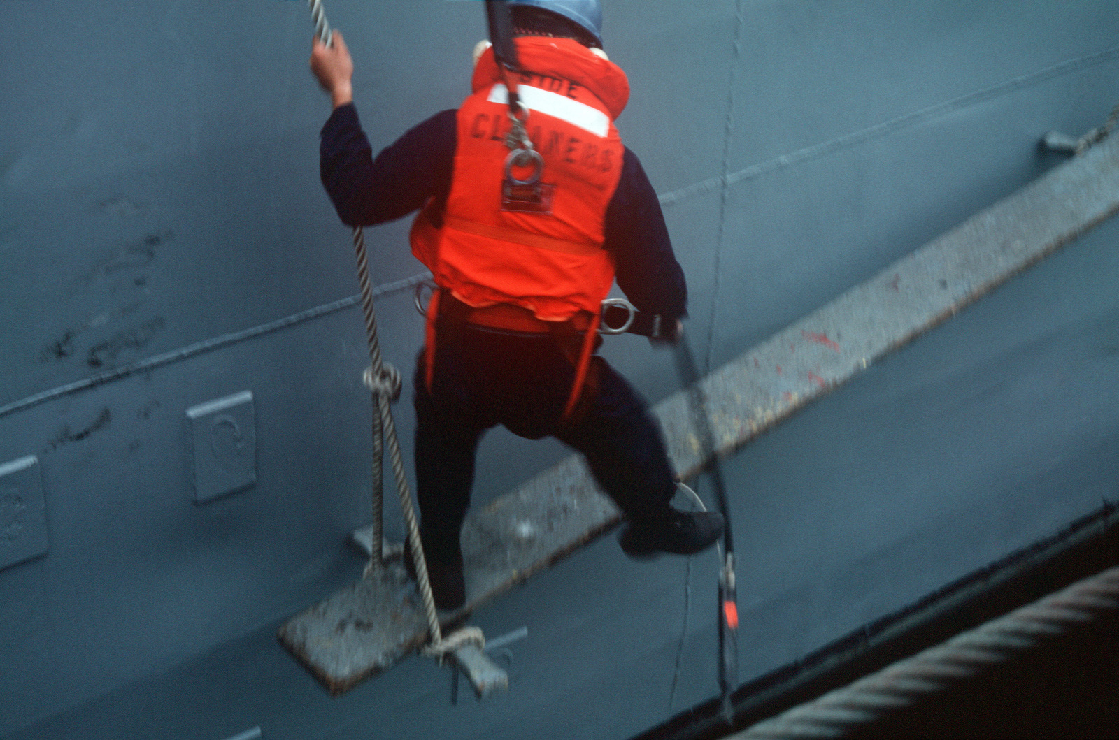 a-crewman-stands-on-a-platform-while-cleaing-the-side-of-the-destroyer