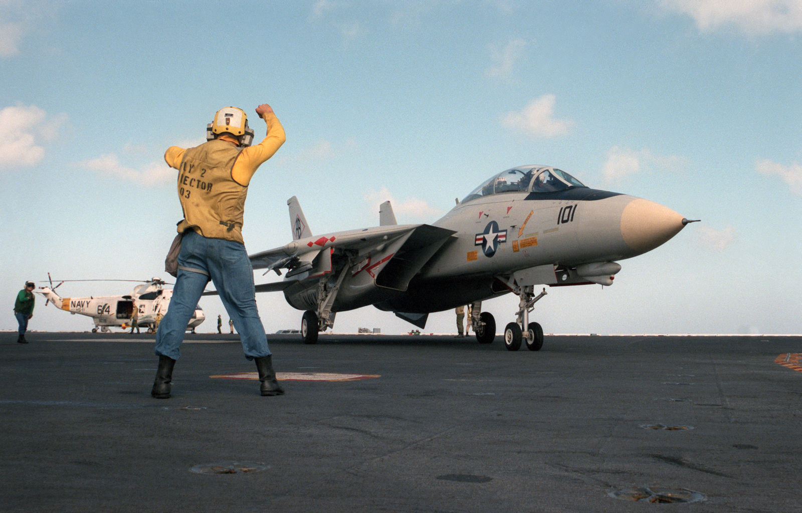 A plane director guides an F-14 Tomcat aircraft into position for ...