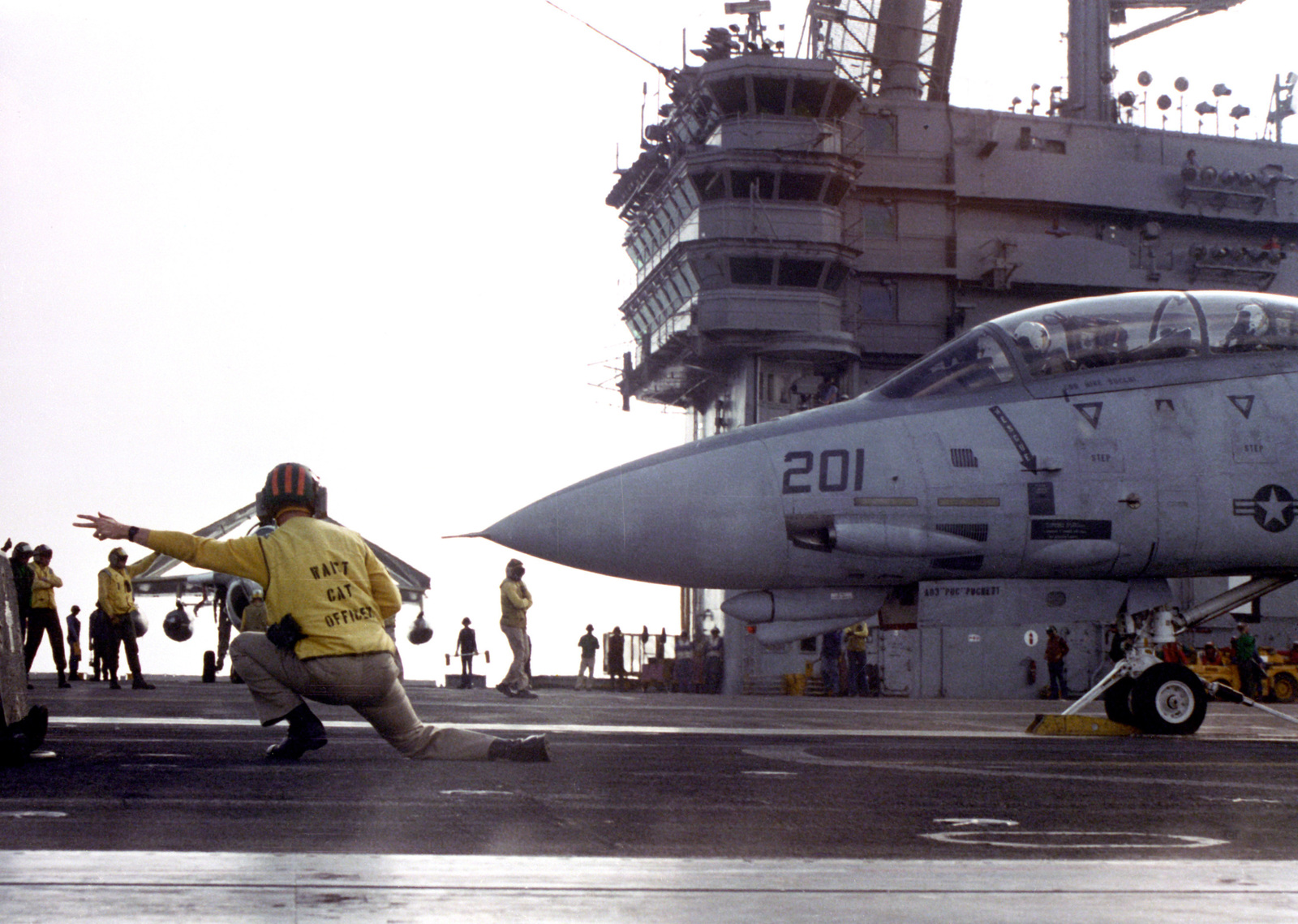 A catapult officer gives the launch signal to the pilot of an F-14A ...