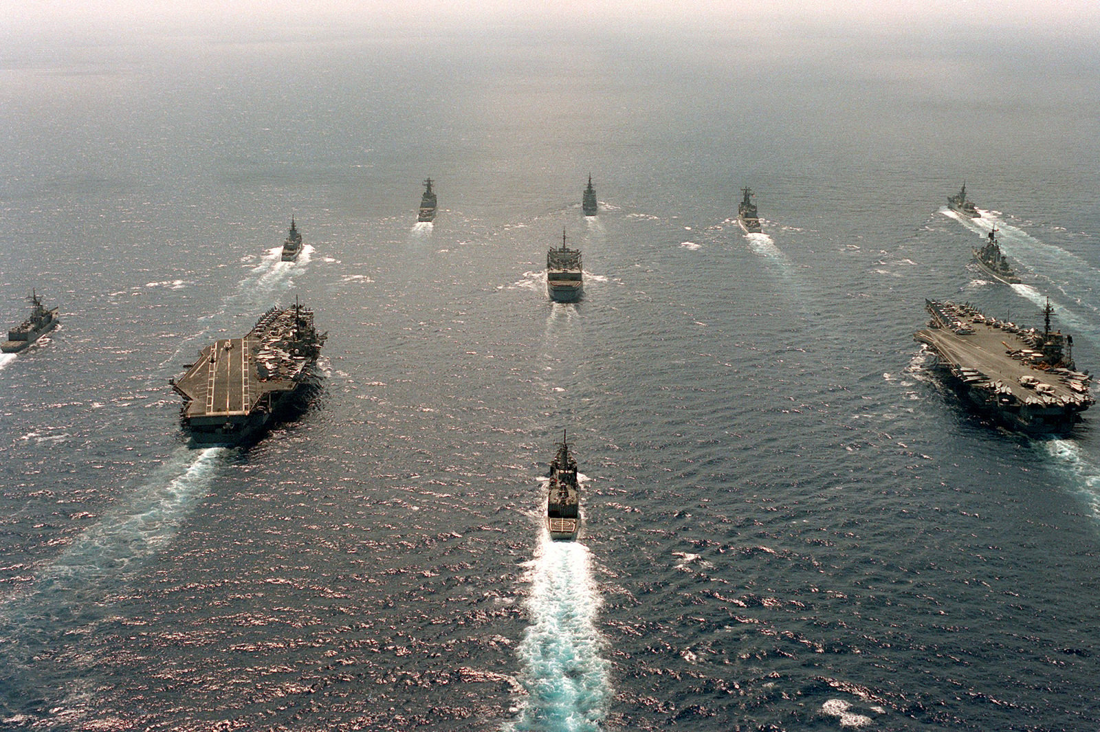 An aerial view of various ships underway in formation. They are ...