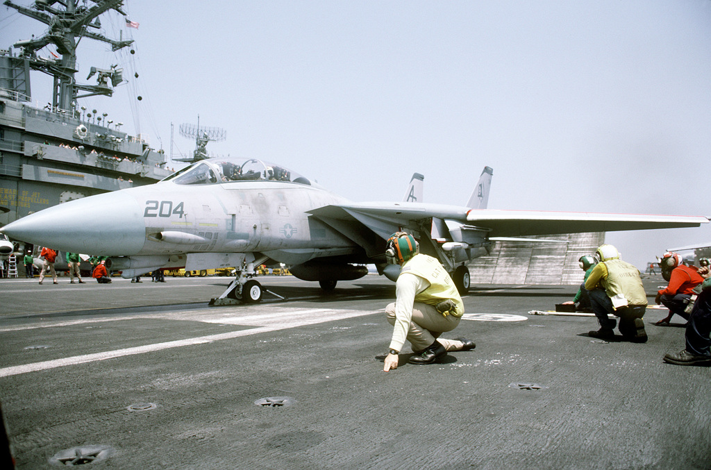 Flight deck crewmen prepare an F-14A Tomcat aircraft for launching from ...
