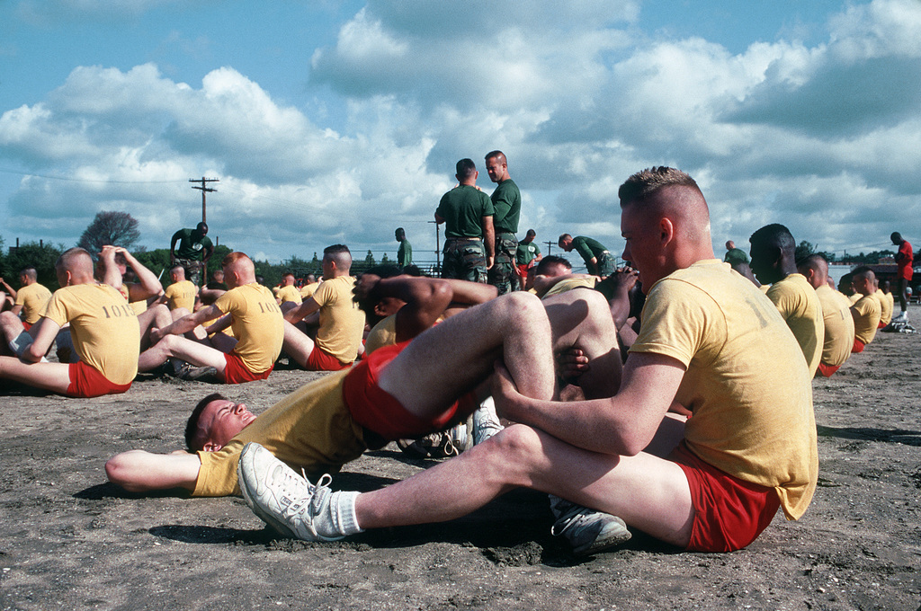 A Marine Corps recruit holds another recruits legs while he