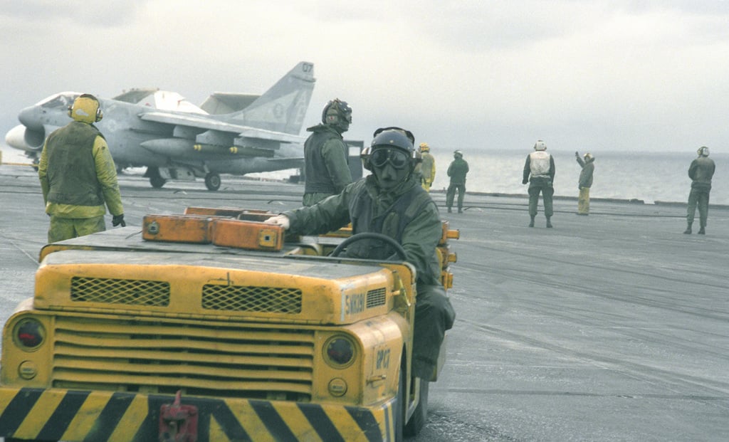 An aircraft handler drives an MD-3A tow tractor across the flight deck ...