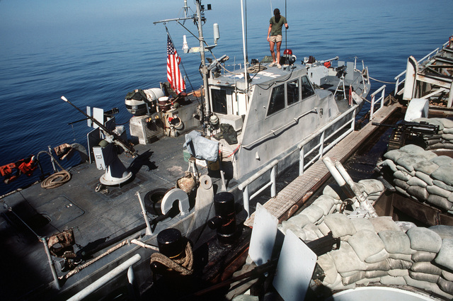 A crewman stands atop the cabin of a PB Mark III patrol boat tied up to ...