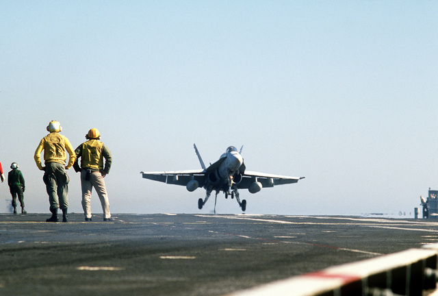 Flight deck crewmen watch an F/A-18 Hornet aircraft touch down on the ...