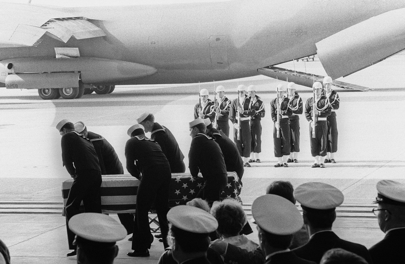 A Navy honor guard stands at present arms as pallbearers pass by ...