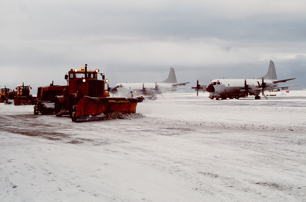 Heavy equipment removing snow moves down the flight line in front of a ...