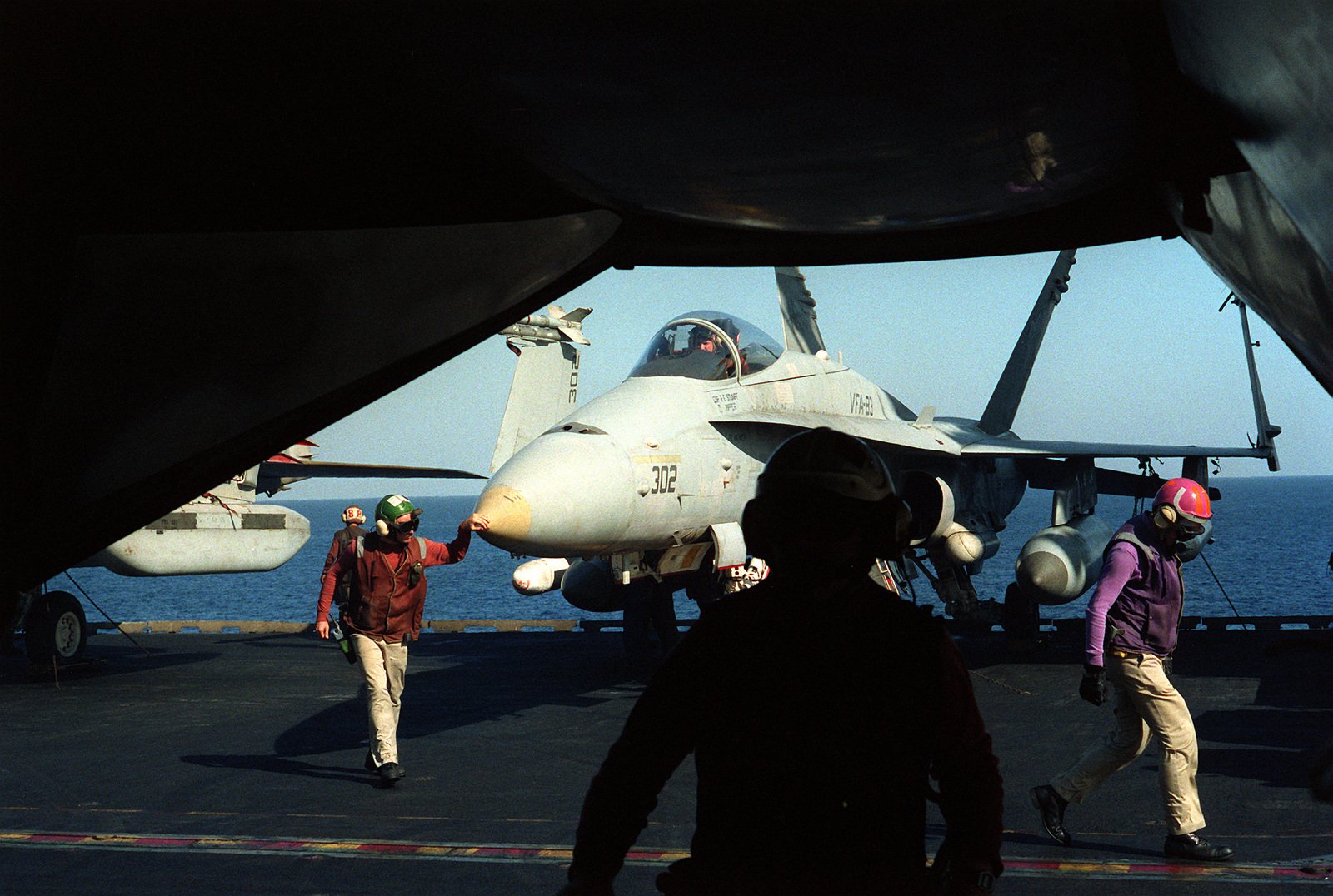 Flight deck crew members conduct preflight checks on a Strike Fighter ...