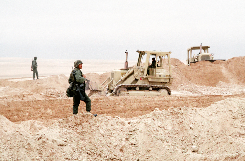 Two armed Seabees keep watch as bulldozers level a plot of ground for a ...