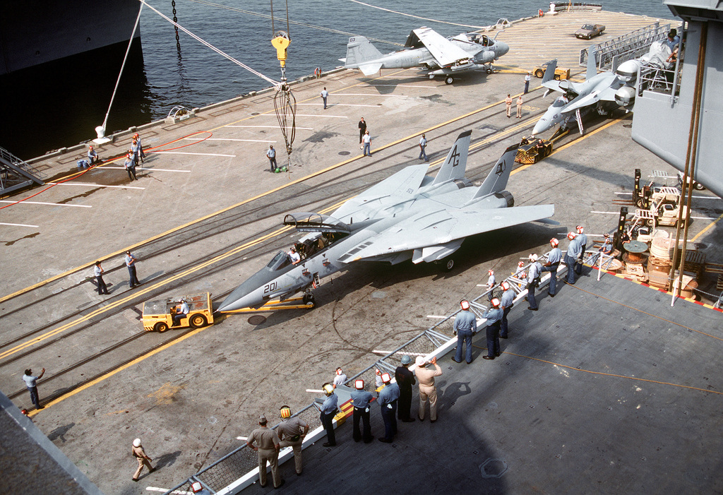 An Md 3a Tow Tractor Positions A Fighter Squadron 142 Vf 142 F 14a Tomcat Aircraft On The Pier As The Plane Is Readied For Lifting By Crane Onto The Nuclear Powered Aircraft Carrier Uss George