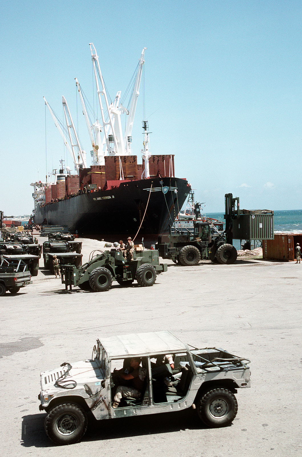 An M998 High Mobility Multipurpose Wheeled Vehicle Hmmwv Drives Past Equipment Being Unloaded From The Pre