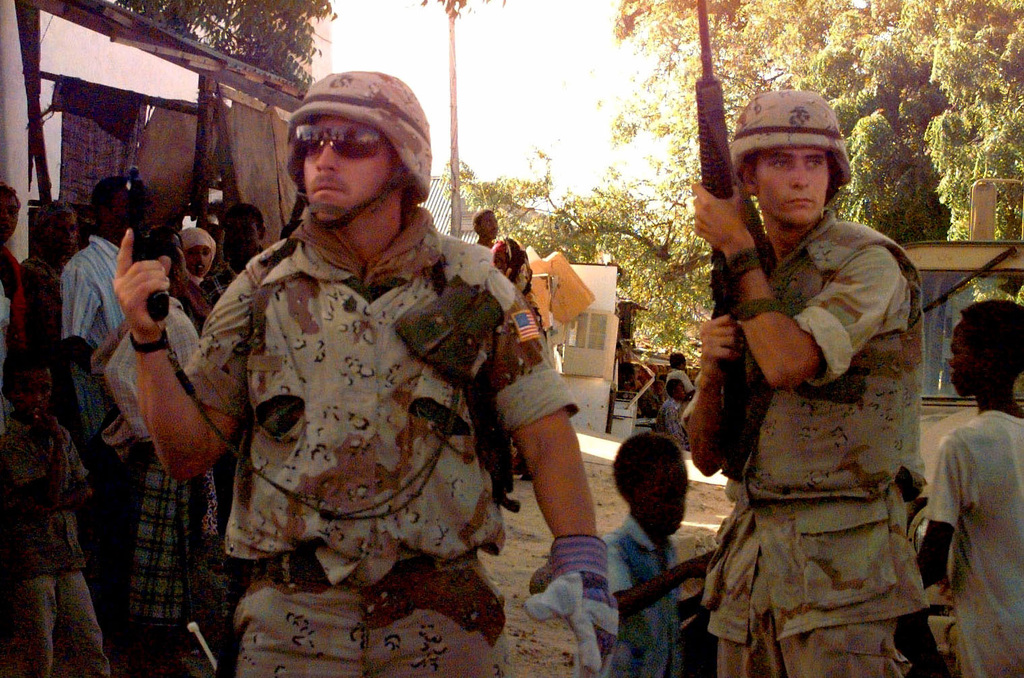 Two US Marines face the camera with weapons drawn. The Marine at left ...