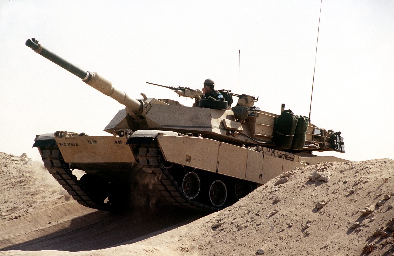 A M1A1 Abrams tank breaches a berm in the desert during maneuvers ...