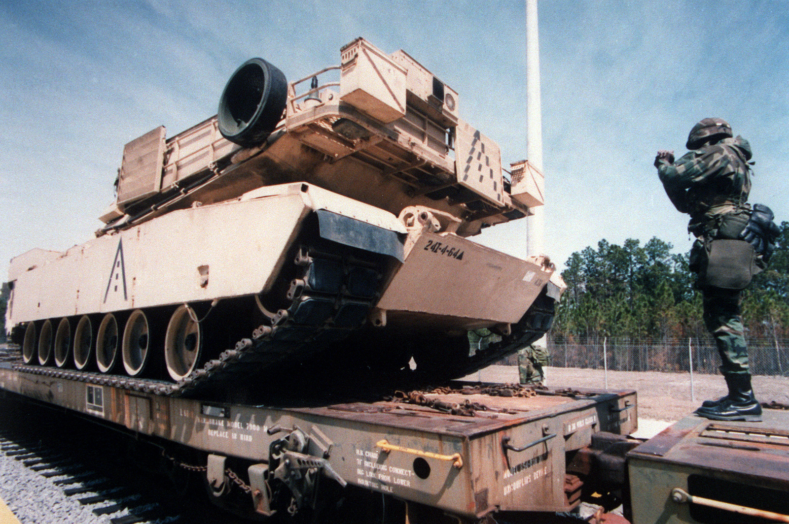 A 3/4 left rear view of an M-1 Abrams Tank being guided onto a railcar ...