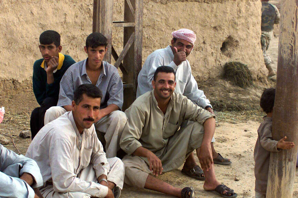 Next to their homes, Iraqi men watch US Marine Corps (USMC) activities ...