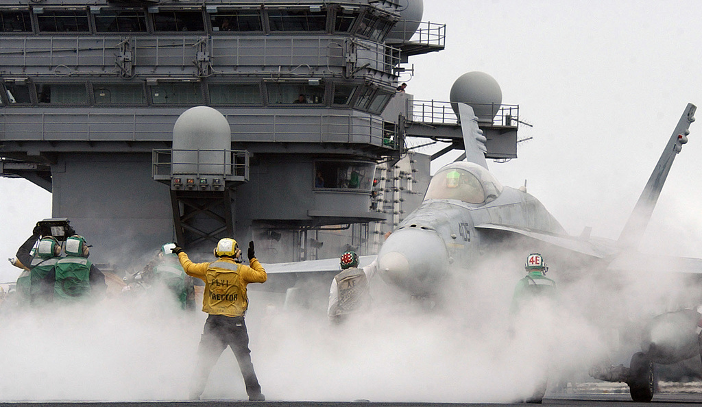 A US Navy (USN) aircraft handler signals a USN F/A-18C Hornet fighter ...