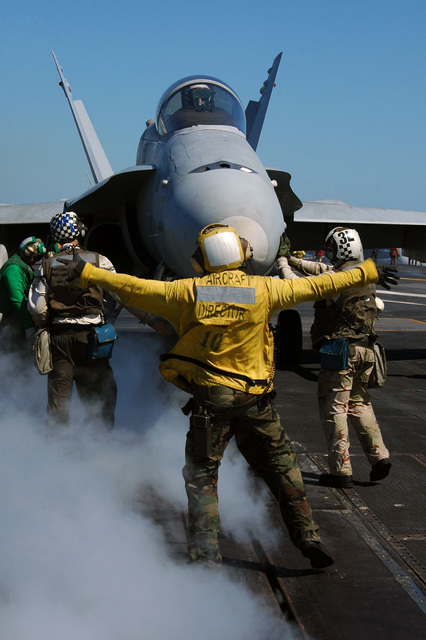 A U.S. Navy aircraft director guides an F/A-18C Hornet aircraft from ...